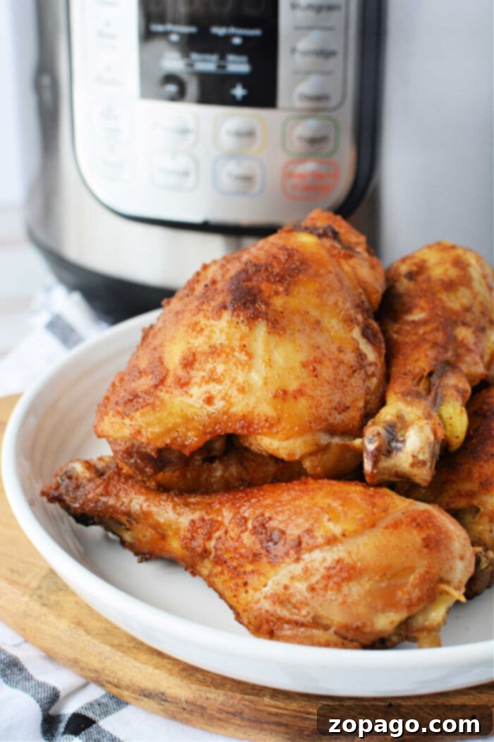 Crispy Pressure Cooker Fried Chicken 7 Cooked, seasoned chicken drumsticks rest enticingly on a white plate in front of an Instant Pot, offering a glimpse into the world of pressure cooker marvels.