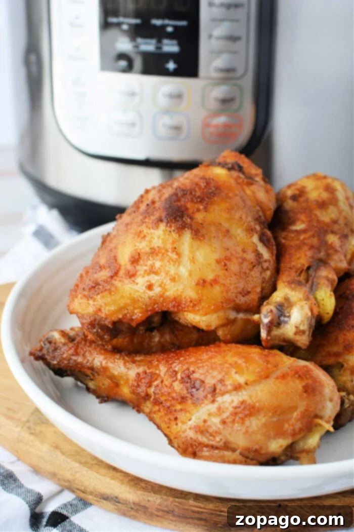 Speedy Pressure Fried Chicken 7 Cooked, seasoned chicken drumsticks rest enticingly on a white plate in front of an Instant Pot, offering a glimpse into the world of pressure cooker marvels.