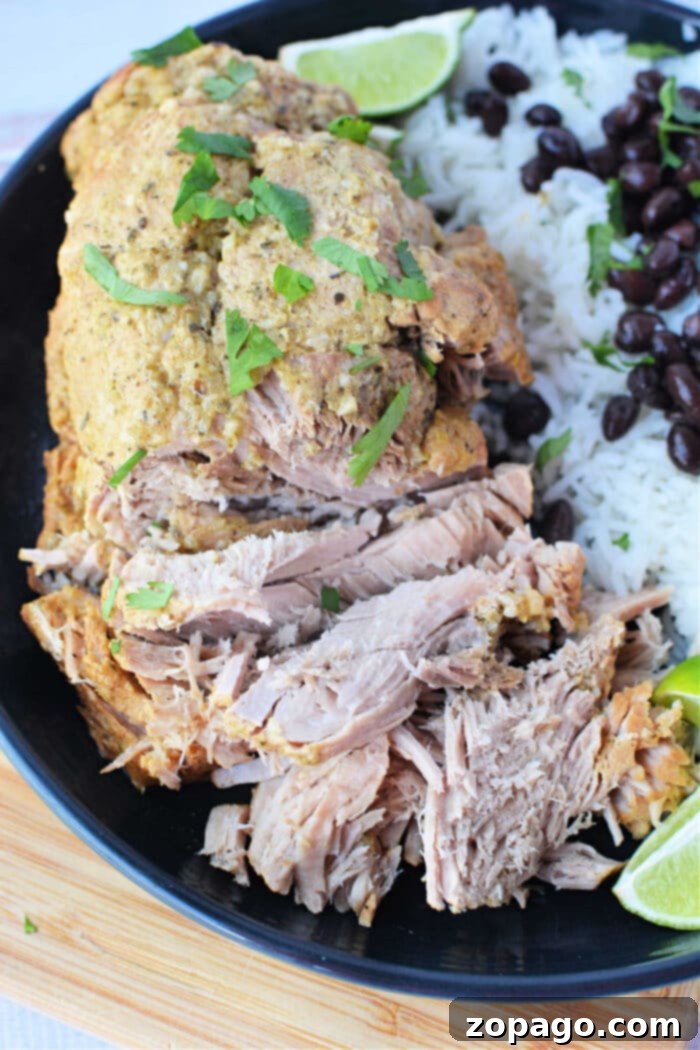 Perfectly Roasted Pork Sirloin 2 Savor shredded pork with herbs, paired perfectly with white rice and black beans, all garnished with lime wedges on a black plate—an exquisite roast recipe for any culinary enthusiast.