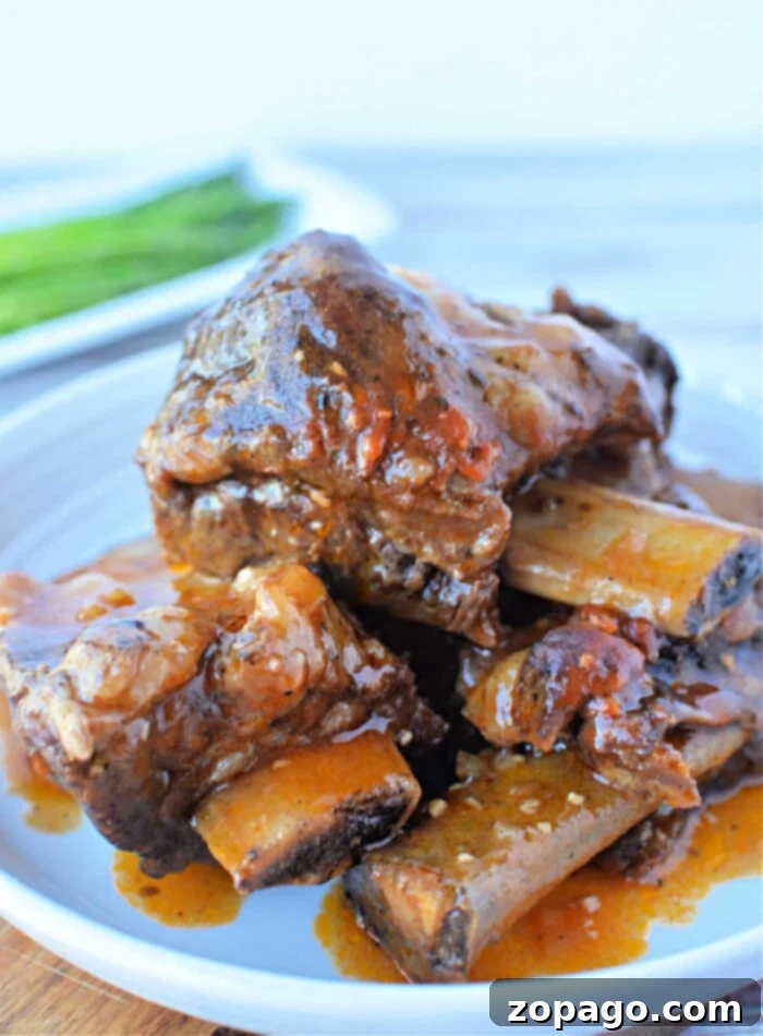 Tender Beef Ribs in the Instant Pot 2 Close-up of a plate featuring mouthwatering braised beef short ribs, simmered to perfection in a pressure cooker and garnished with a rich red sauce, all elegantly presented on a white plate.