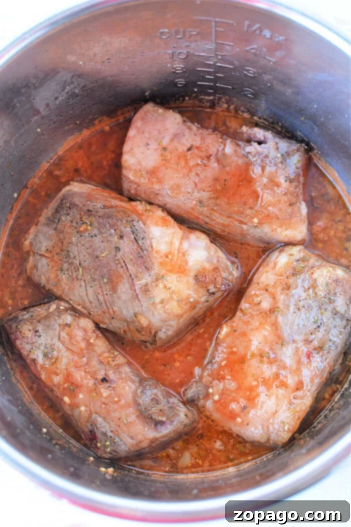 Tender Pressure Cooker Beef Ribs 4 Tender beef ribs simmer in a rich red sauce inside a stainless steel pot, infusing each bite with mouthwatering flavor.