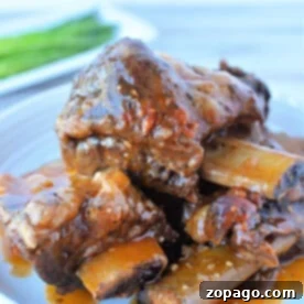 Close-up of a plate featuring mouthwatering braised beef short ribs, simmered to perfection in a pressure cooker and garnished with a rich red sauce, all elegantly presented on a white plate.