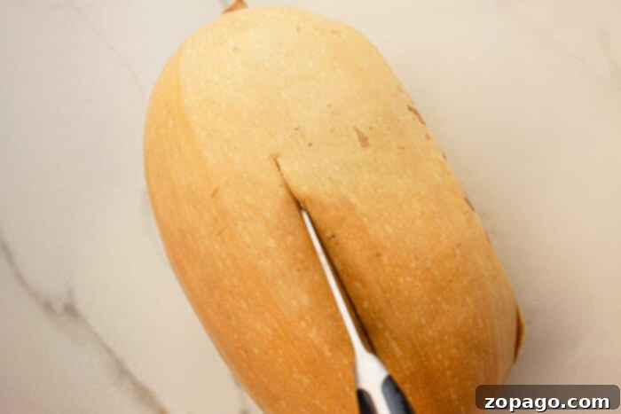 Effortless Slow Cooker Spaghetti Squash 5 A butternut squash being sliced with a knife on a light-colored countertop, ready to transform into a delicious slow cooker spaghetti squash dish.
