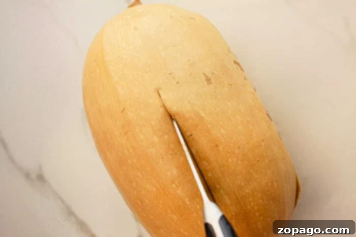 Effortless Slow Cooker Spaghetti Squash 5 A butternut squash being sliced with a knife on a light-colored countertop, ready to transform into a delicious slow cooker spaghetti squash dish.