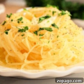 Effortless Slow Cooker Spaghetti Squash 7 A slow cooker spaghetti squash sits on the plate, enhanced by a parsley garnish and a sprinkle of black pepper.