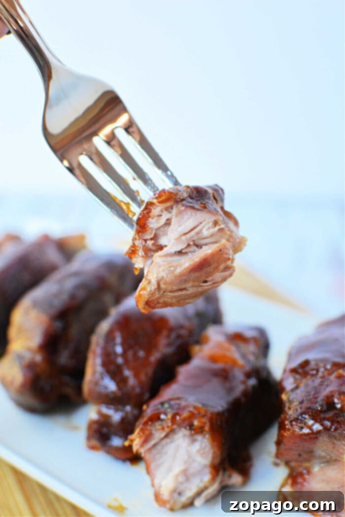 Baked Boneless Pork Ribs 5 A fork holding a piece of glazed, tender boneless pork ribs above a plate of ribs, showcasing the perfect result of oven cooking.