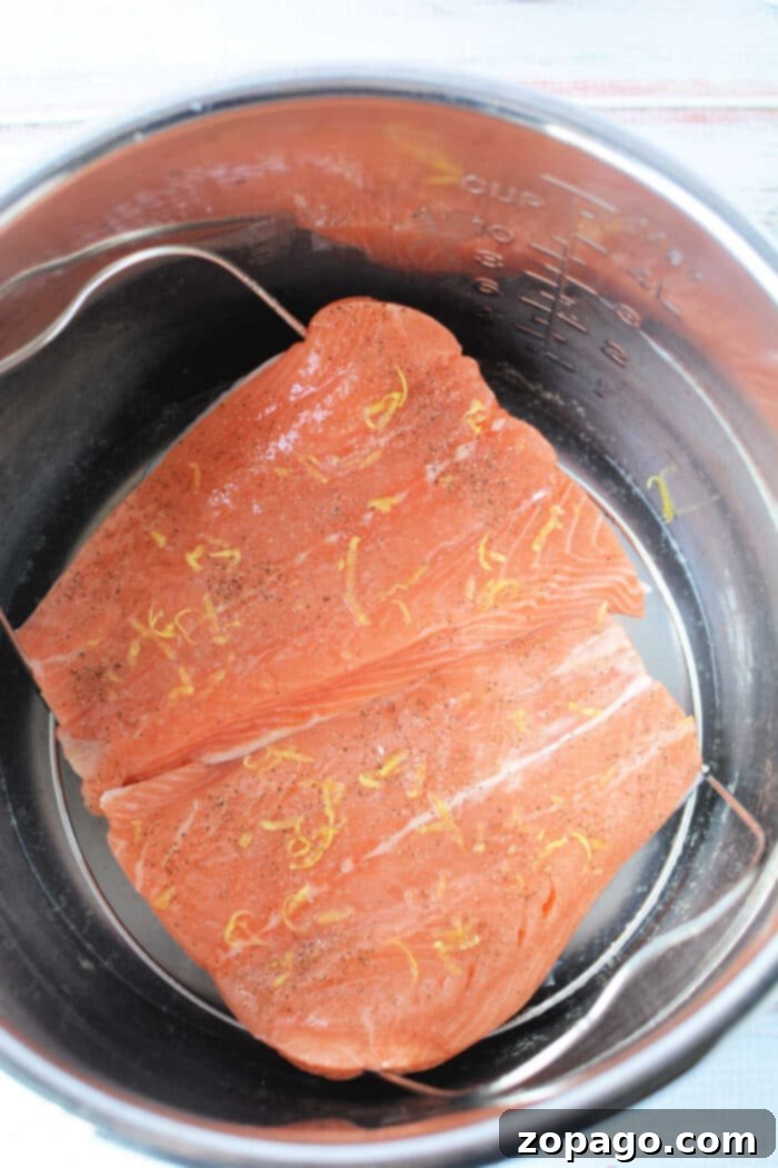 Quick Pressure Cooker Salmon 5 Raw salmon fillets with lemon zest and pepper, nestled in a pressure cooker for a quick and flavorful meal.