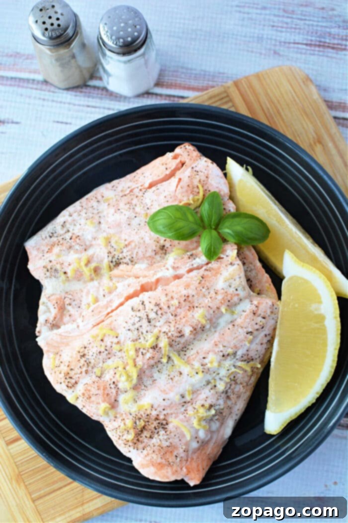 Quick Pressure Cooker Salmon 7 Salmon fillets with lemon zest and basil on a black plate, served alongside lemon wedges, salt, and pepper shakers. Perfectly tender, these fillets could easily be mistaken for being made in a pressure cooker.