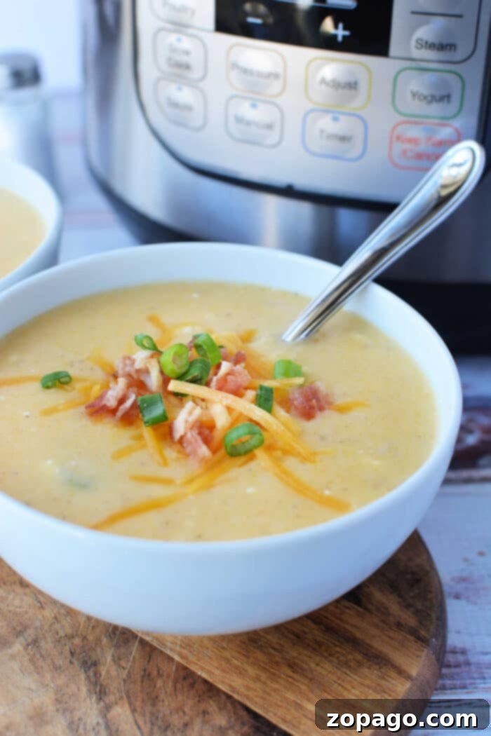 A bowl of creamy potato soup topped with cheese, crispy bacon, and green onions sits invitingly with a spoon beside it, fresh from the pressure cooker.