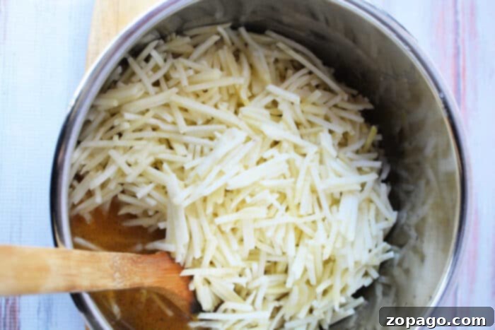 Creamy Instant Pot Hash Brown Potato Soup 4 A large pot filled with a mound of shredded potatoes, the key ingredient for delicious homemade hash browns, rests on a rustic wooden surface next to a wooden spoon.