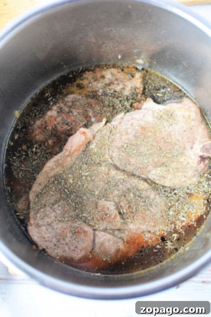 Perfect Pork Steaks 5 Two raw pork steaks with fresh herbs and a rich broth in a metal pot, ready to be cooked for a simple yet delicious pork steak recipe.