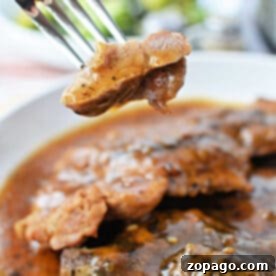 A fork holds a bite of tender meat above a plate of saucy, seasoned pork steak, showcasing a mouthwatering pork steak recipe.