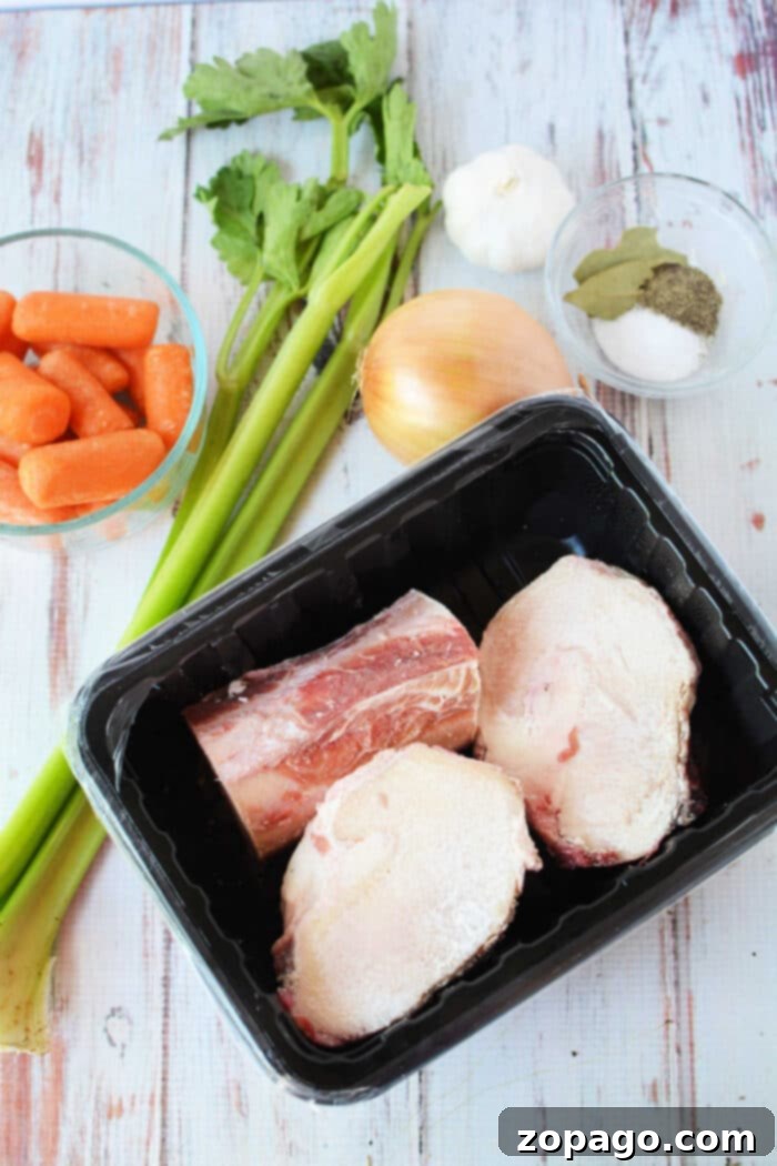 Effortless Slow Cooker Bone Broth 3 Ingredients for bone broth: celery, carrots, garlic, and onion lay next to beef bones on a tray. A bowl of spices with bay leaves completes the setup. Perfectly suited for a slow cooker, these elements promise depth and warmth in every sip.