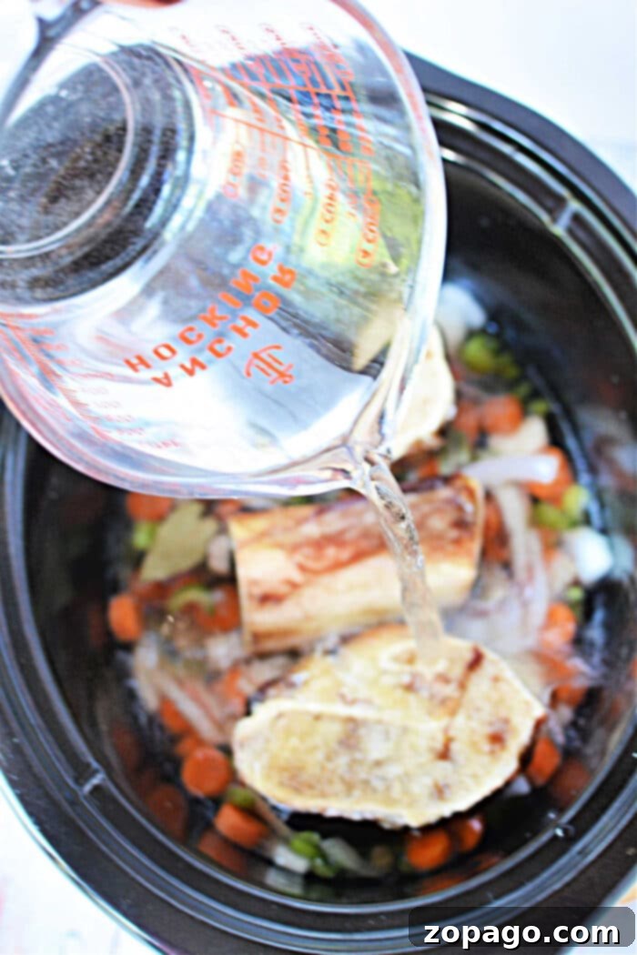 Effortless Slow Cooker Bone Broth 5 Pouring water into a slow cooker, creating a rich bone broth with vegetables and bones.