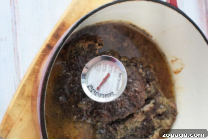 A succulent Stove Top Pot Roast sits in a pot on a wooden surface, with a thermometer revealing its perfect temperature of 150 degrees Fahrenheit.