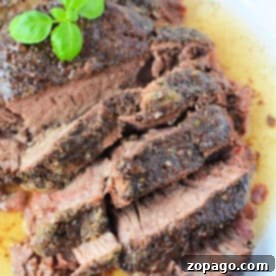 Slices of seasoned roast beef, reminiscent of a classic stove top pot roast, are topped with fresh basil on a white plate, surrounded by rich meat juices.