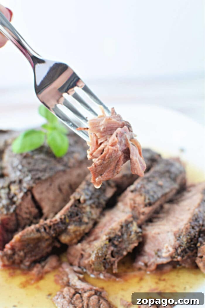 Easy Stovetop Pot Roast 7 A fork holds a piece of sliced, cooked Stove Top Pot Roast above a plate of beef, garnished with a basil leaf.