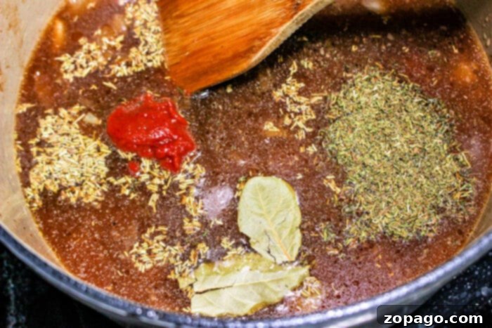 Tender Braised Chuck Roast 4 A cooking pot simmers with rich broth, herbs, bay leaves, and tomato paste. A wooden spoon stirs the ingredients into a fragrant harmony, ideal for braising with chuck roast and a splash of red wine.