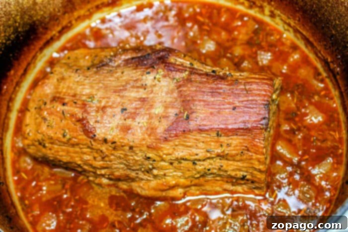 Tender Braised Chuck Roast 5 A succulent chuck roast braised to perfection in a pan, enveloped in a rich, brown sauce infused with red wine and adorned with visible herbs and spices.