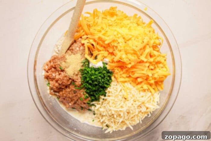 Easy Instant Pot Sausage Balls 4 Ingredients in a bowl: shredded cheese, herbs, ground meat, and cream mix enticingly, ready to transform into savory sausage balls. A wooden spoon rests on the side, waiting to blend the flavors under the gentle guidance of a pressure cooker.