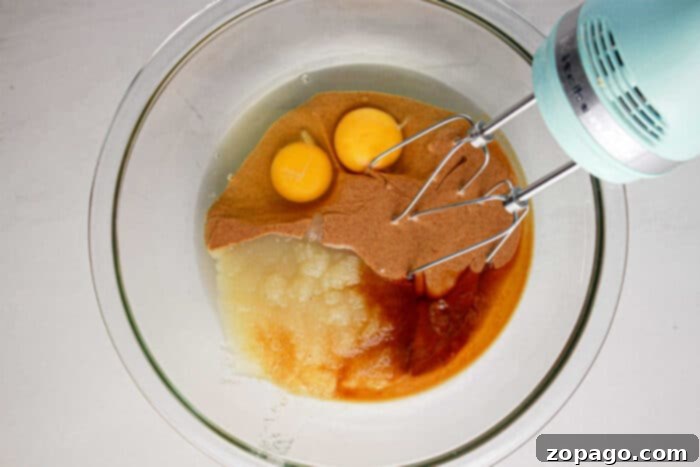 High-Protein Brownie Bites 4 A kitchen mixer stands ready over a glass bowl, filled with a smooth, rich batter of eggs and applesauce, poised for mixing into a delicious protein brownie recipe.