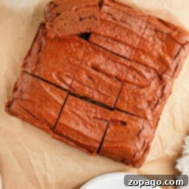 High-Protein Brownie Bites 5 A rich, sliced brownie sits invitingly on parchment paper, a white plate poised nearby, with a hint of greenery in the corner, highlighting this delightful, healthy protein brownie.