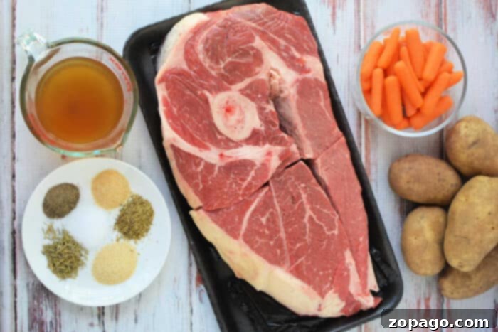 Perfect Slow Cooker Arm Roast 3 Raw chuck roast, baby carrots, potatoes, broth, and assorted spices—perfect ingredients for a comforting slow cooker meal—are arranged on a white wooden surface.