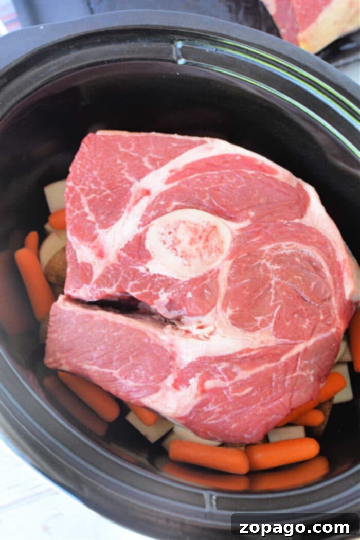 Perfect Slow Cooker Arm Roast 4 Arm Roast nestled atop carrots and potatoes inside a black Slow Cooker, making this Arm Roast Recipe both hearty and convenient.