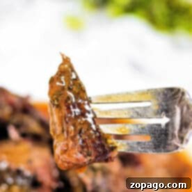 A close-up of a fork holding a juicy, glazed piece of arm roast with herbs—a delicious result from a slow cooker.