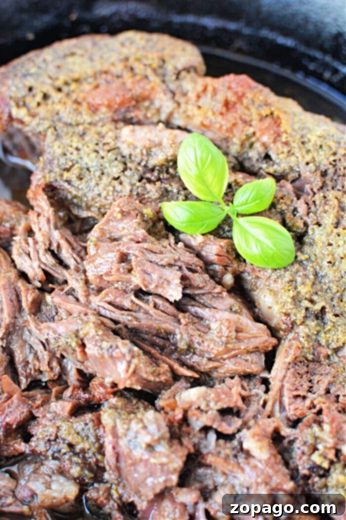 Melt-in-Your-Mouth Boneless Chuck Roast 2 A close-up of perfectly cooked boneless beef topped with fresh green basil leaves, showcasing its incredible tenderness and succulent texture.