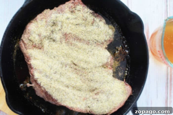 Melt-in-Your-Mouth Boneless Chuck Roast 5 A seasoned boneless beef cut perfectly seared in a cast-iron skillet, resting enticingly beside a measuring cup filled with aromatic liquid, ready for slow cooking.