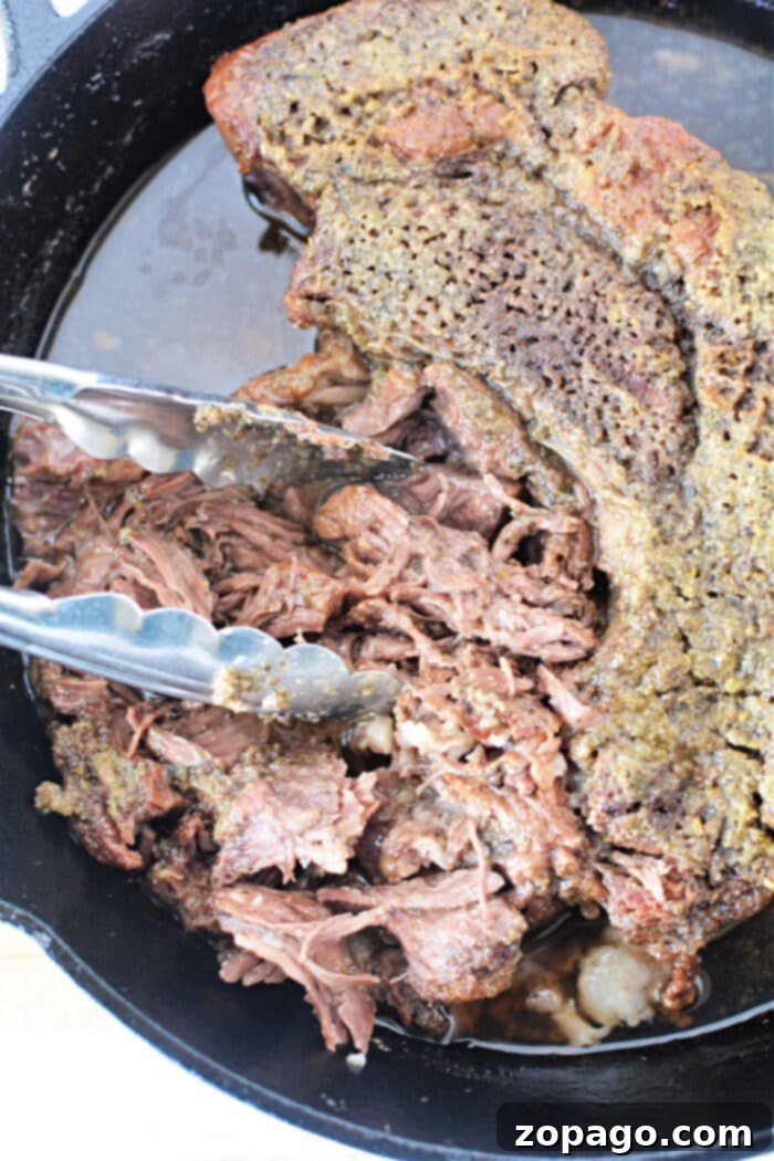 Melt-in-Your-Mouth Boneless Chuck Roast 6 Boneless pot roast shredded with tongs in a cast iron skillet, ready to be served or incorporated into a delicious meal.