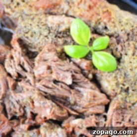 Melt-in-Your-Mouth Boneless Chuck Roast 7 A close-up of perfectly cooked boneless beef topped with fresh green basil leaves.