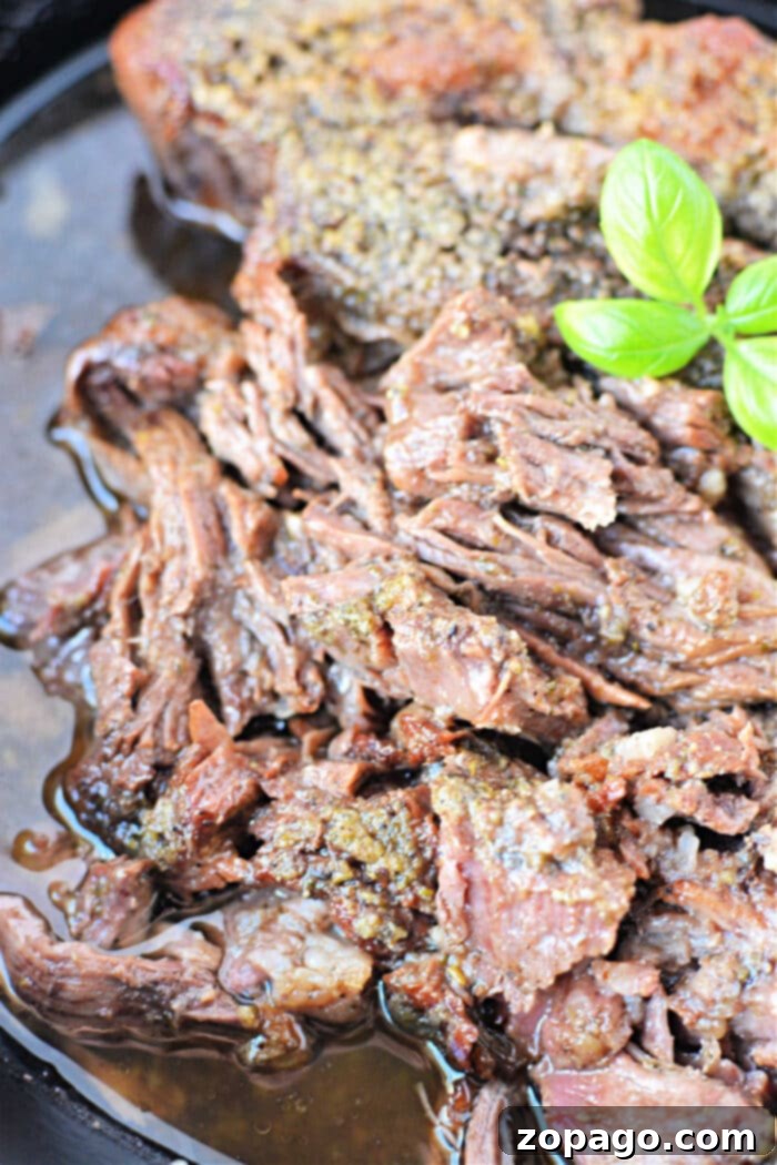 Melt-in-Your-Mouth Boneless Chuck Roast 8 Close-up of shredded boneless chuck roast in its rich sauce, adorned with a garnish of fresh green basil leaves, presented as a delicious meal.