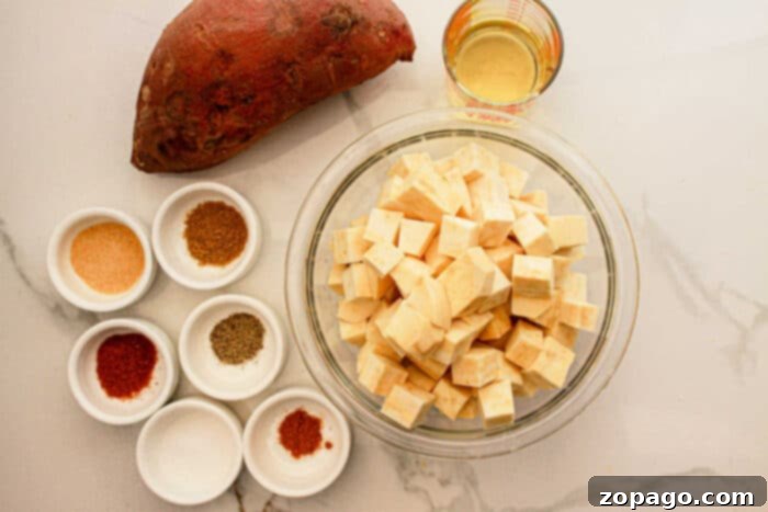 Creamy White Sweet Potato Delight 3 Cubed white sweet potatoes in a bowl, a whole white sweet potato, oil, and spices in small bowls on a white surface—perfect for your next delicious White Sweet Potato Recipe.
