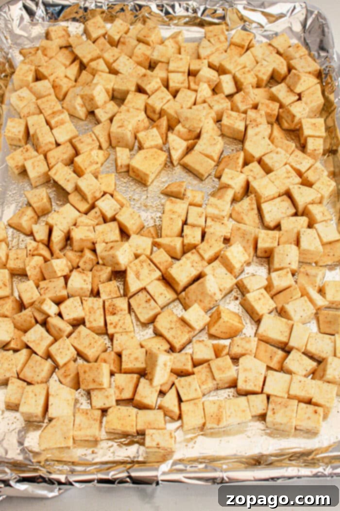 Irresistible White Sweet Potato Recipes 5 Cubed sweet potato seasoned and spread evenly on a foil-lined baking sheet, prepared for baking. This image captures a key step in creating a delicious and protein-packed White Sweet Potato Recipe.