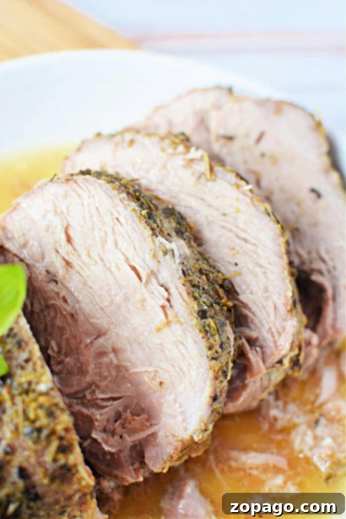 Tender Slow Cooker Porketta 2 Sliced roasted porketta seasoned with herbs served on a white plate, garnished with a basil leaf.