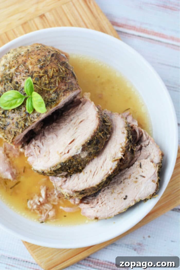 Tender Slow Cooker Porketta 7 Enjoy a deliciously tender Crockpot Porketta Roast, perfectly herb-crusted and sliced, served with rich gravy on a white plate. Garnished with fresh basil for an added touch of flavor.