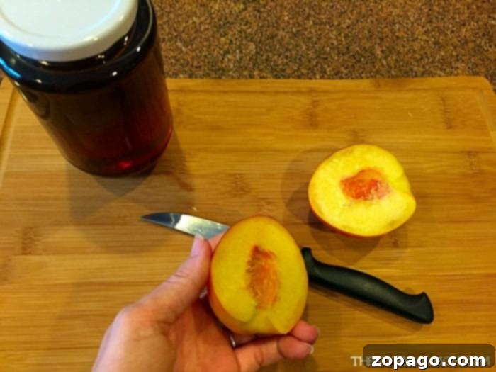 A hand holds a sliced peach on a wooden cutting board, next to a knife and a jar, ready for preparing grilled peaches as a delicious BBQ dessert.