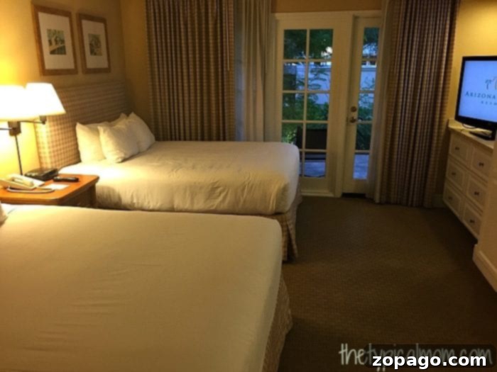 Arizona Grand Resort A Comprehensive Review 2 The Arizona Grand Resort offers a hotel room featuring two double beds, a nightstand with a lamp, and a dresser. A glass door with curtains opens to a patio with a serene garden view.