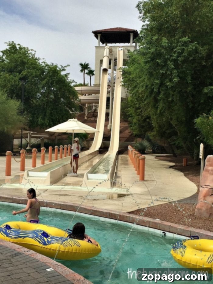 A Look Inside the Arizona Grand Resort 5 Two people in yellow inflatable rings float along a lazy river at Arizona Grand Resort, nestled at the bottom of two tall water slides. A lifeguard stands watch as trees and umbrellas create a serene oasis around the attraction.