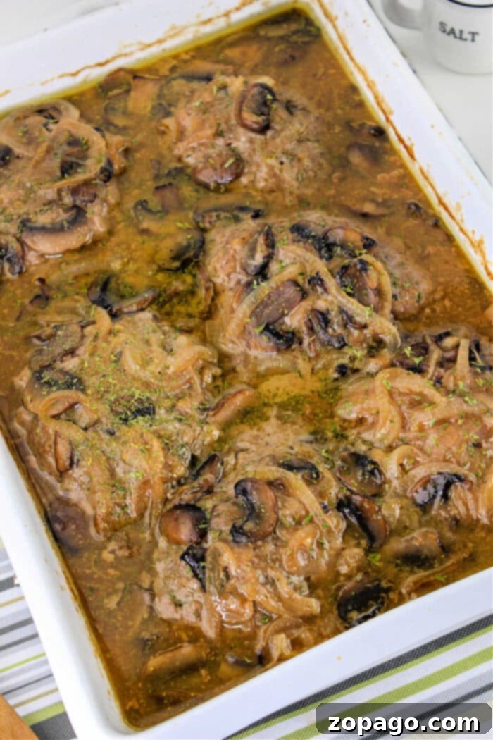 Salisbury Steak 2 Baked hamburger steak in gravy with mushrooms and onions, reminiscent of classic Hamburger Steak flavors, served in a white casserole dish.