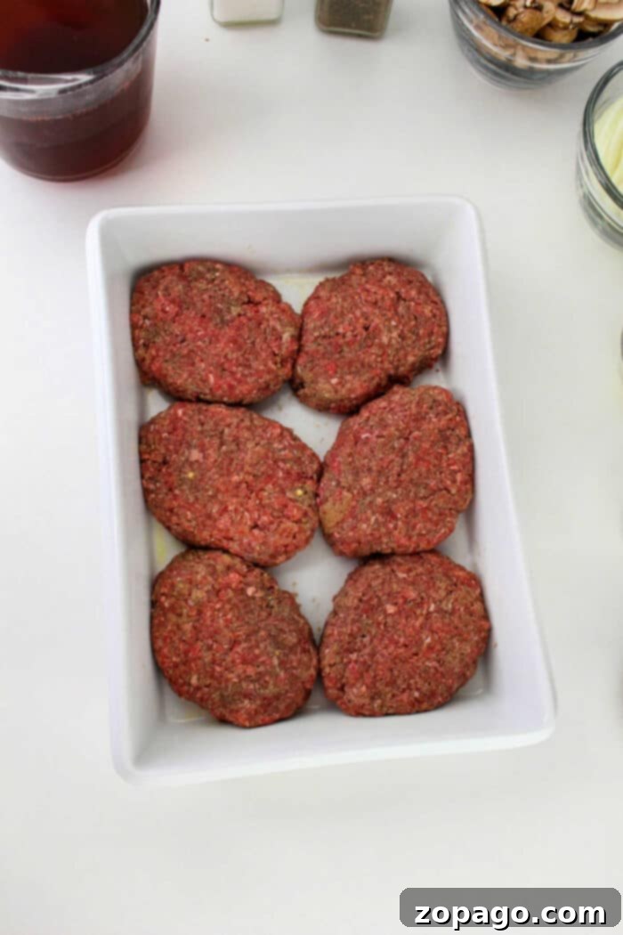 Salisbury Steak 5 Six raw ground beef patties, perfect for making Hamburger Steak, are arranged in a white rectangular dish on a white surface.