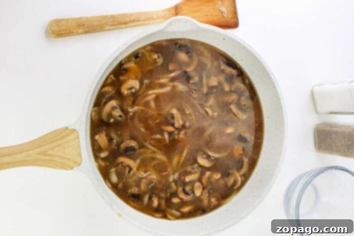 Salisbury Steak 6 A white skillet filled with savory mushroom and onion gravy for Hamburger Steak, next to a wooden spatula, salt, and pepper shakers.