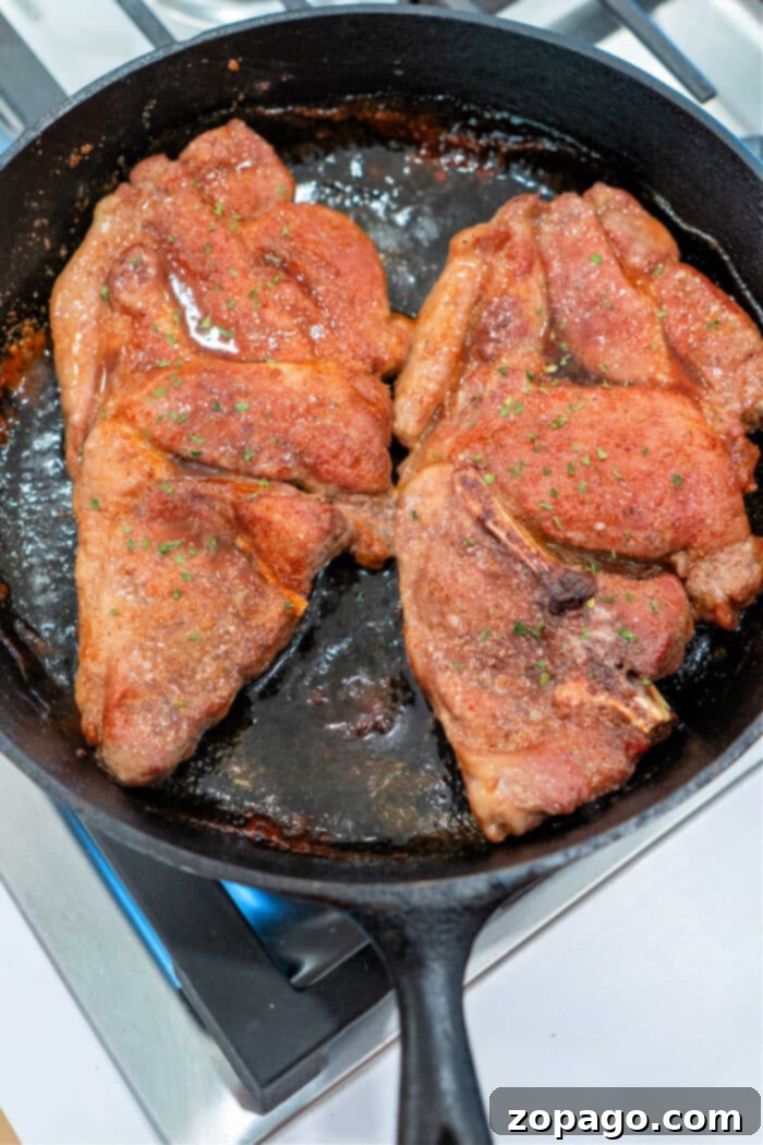 Hearty Pork Shoulder Steak 7 Two beautifully seasoned pork shoulder steaks sizzling in a black cast iron skillet on a stovetop, creating a perfect crust.