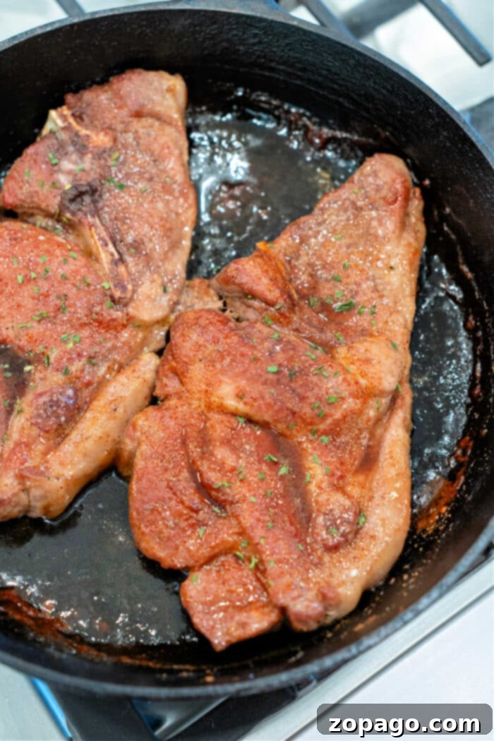 Hearty Pork Shoulder Steak 8 Two perfectly seasoned and seared pork shoulder steaks sizzling in a cast iron skillet on a stovetop, indicating ideal doneness before resting.