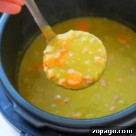 A ladle of crock pot express split pea soup with carrots and ham held over a pot.
