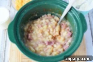 Creamy Slow Cooker Loaded Baked Potato Soup 4 A crockpot brimming with loaded baked potato soup features creamy diced potatoes and savory ham, with a metal spoon nestled inside.