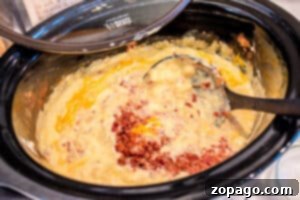 Creamy Slow Cooker Loaded Baked Potato Soup 5 A slow cooker filled with creamy Hashbrown Soup, shredded cheese, and crumbled bacon being stirred with a ladle.