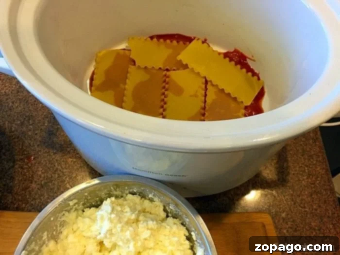 Layers of uncooked lasagna noodles, sauce, and cheese in a slow cooker. Layers of Crockpot Lasagna in a slow cooker.